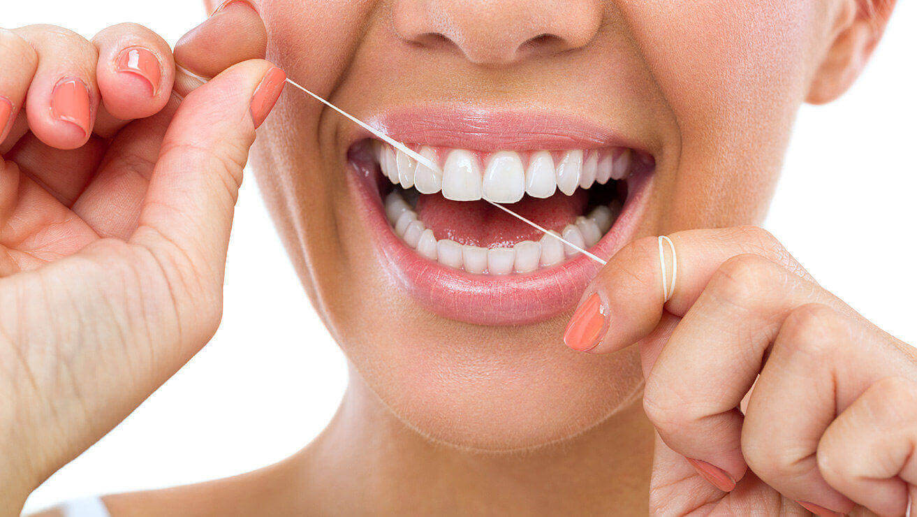 Nő fehér háttér előtt mutatja a helyes fogselyem használatot, a fogselymet az ujjára tekerve az első fogai között<br />